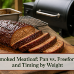 Sliced glazed smoked meatloaf on a rustic board beside a pellet smoker